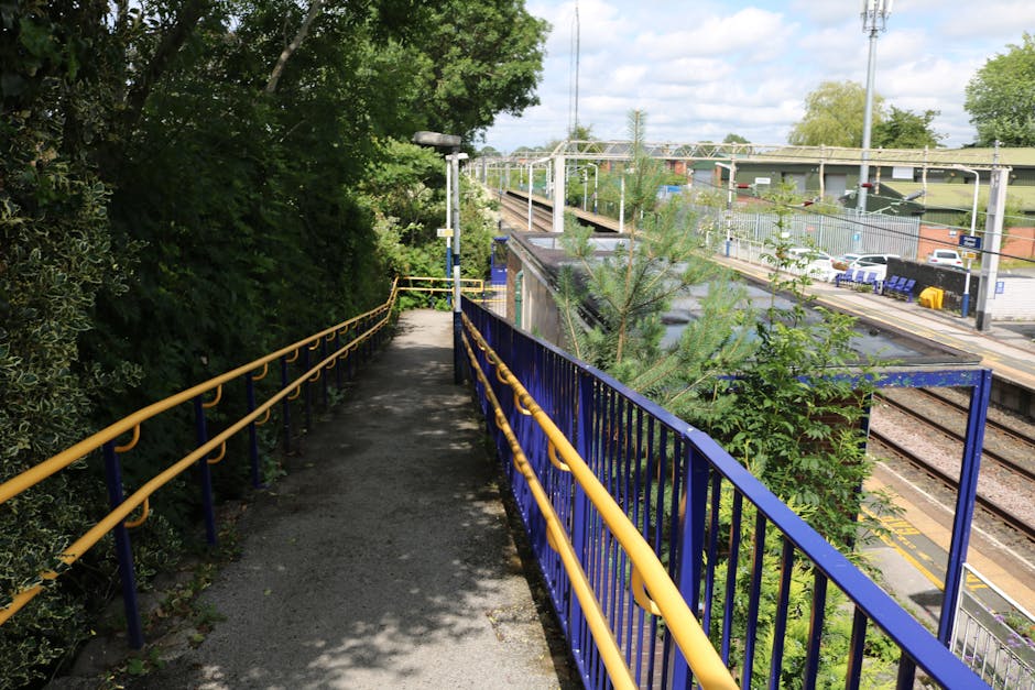A set of metal stairs with wooden treads featuring yellow safety edges, located inside a transport or warehouse facility. The stairs are flanked by yellow handrails on both sides and lead up to an ele